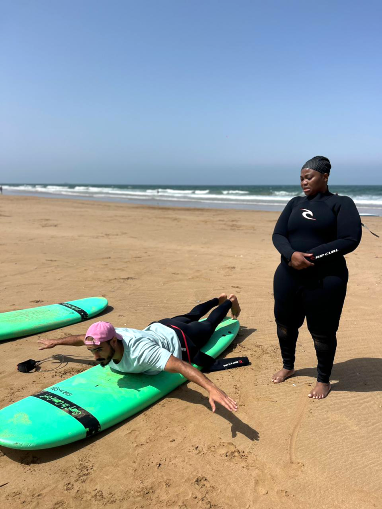 Hatim montrant à une élève femme adulte comment bien se positionner sur une planche de surf lors d’un cours particulier à Tamraght