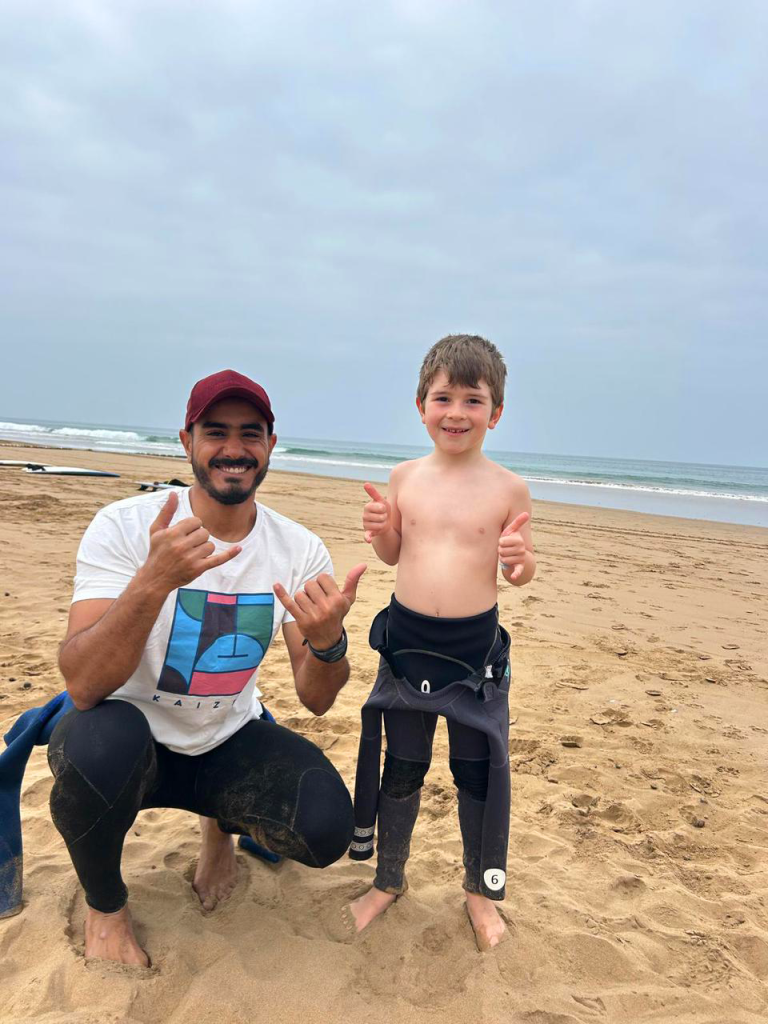 Hatim aidant un enfant de 6 ans à enfiler sa combinaison avant un cours particulier de surf