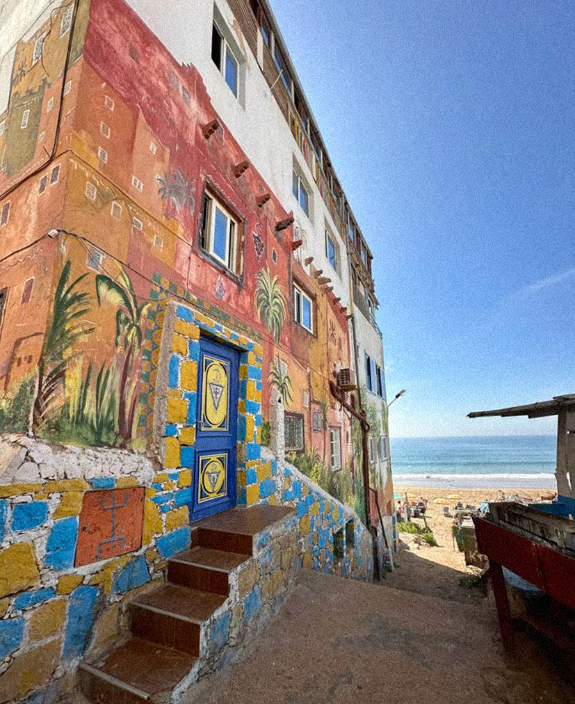 Vue de la plage de Taghazout depuis une rue du village avec un mur coloré typique