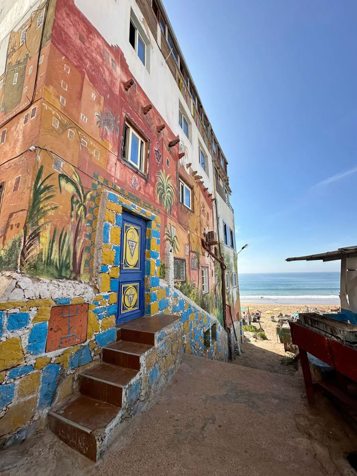 Vue de la plage de Taghazout depuis une rue du village avec un mur coloré typique
